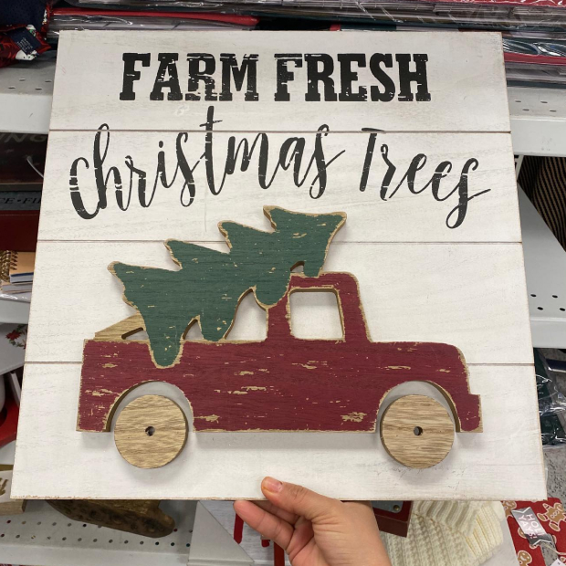 Wooden sign is shown with the words Farm Fresh Christmas Trees, and a wooden red truck carrying a green tree