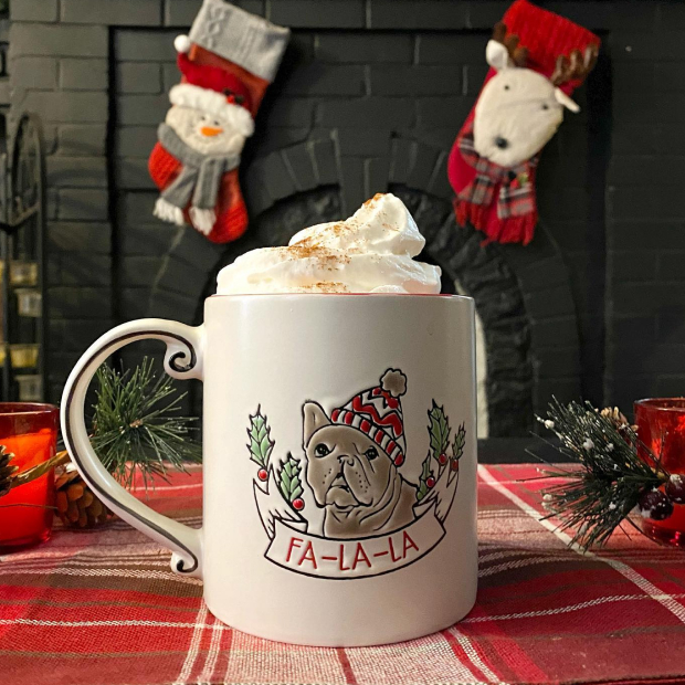 A Christmas mug is shown with hot chocolate and whipped cream and the message "Fa La La La La" in front of two stocking hung on a fireplace