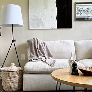 A cozy living room with a floor lamp, a sofa, a coffee table, modern wall arts and a woven storage basket
