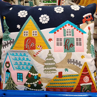 An image displaying an adorable pillow with a Christmas village scene and a Christmas tree design from a Ross store