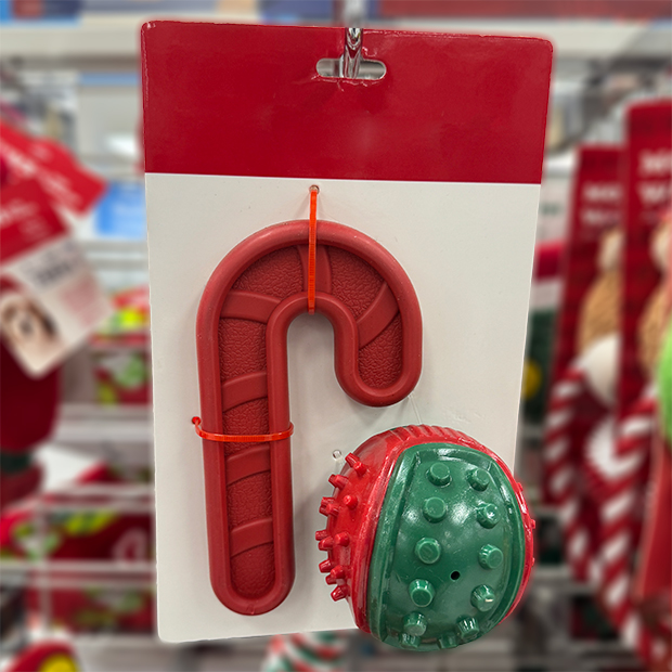 Packaged dog chew toy set featuring a red candy cane-shaped toy and a green textured ball with red accents, displayed on a store shelf.