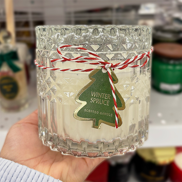 Clear textured glass jar candle with a green tree-shaped tag reading "Winter Spruce" and red-and-white twine bow.