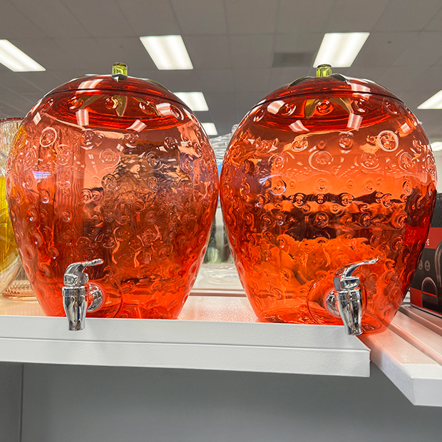 Two round clear strawberries beverage dispensers with a spout.