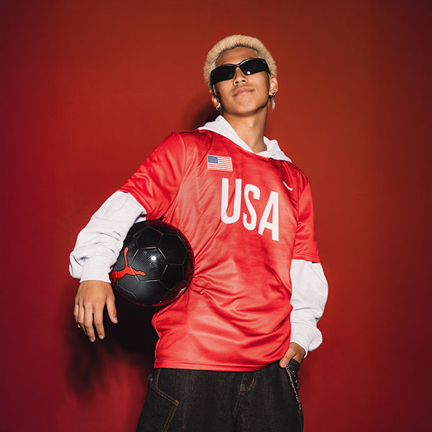 Person in a red USA jersey holding a black soccer ball against a red backdrop.