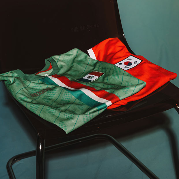 Mexico and South Korea soccer jerseys folded on a chair against a green background.
