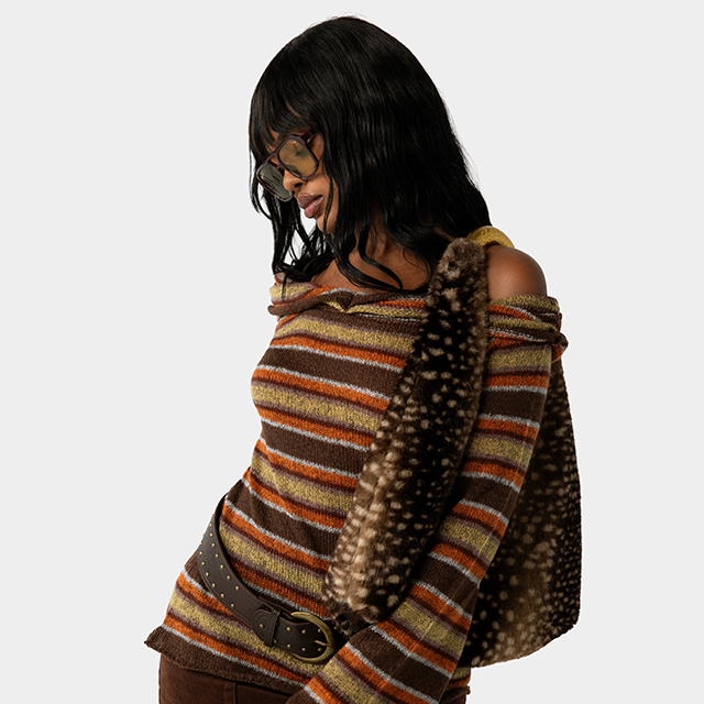 Model wears a striped brown, olive and orange off the shoulder sweater with a fawn printed handbag.